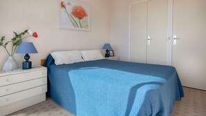 Un dormitorio con una cama, dos mesitas de noche con lámparas, un aparador, un cuadro en la pared y una puerta.