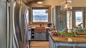 Eine Küche mit einem Edelstahl-Kühlschrank, einer Holzbalkendecke und Bergblick durch ein großes Fenster.