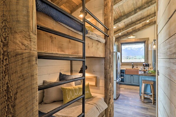 A rustic cabin interior with bunk beds, a kitchen area, and a view of mountains. - Stunning Kalispell Cottage on 30-acre Farm! (Kalispell)