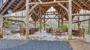 Ein rustikales Holzpavillon mit Steinboden, Holztischen und -stühlen.