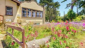 Ein Haus mit einem Garten voller bunter Blumen, einer hölzernen Bank und einem großen Baum.