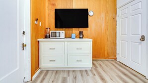 Ein kleiner, sauberer Raum mit einer Holzvertäfelung, einem weißen Schrank, einem Flachbildfernseher, einer Mikrowelle und einer Kaffeemaschine.