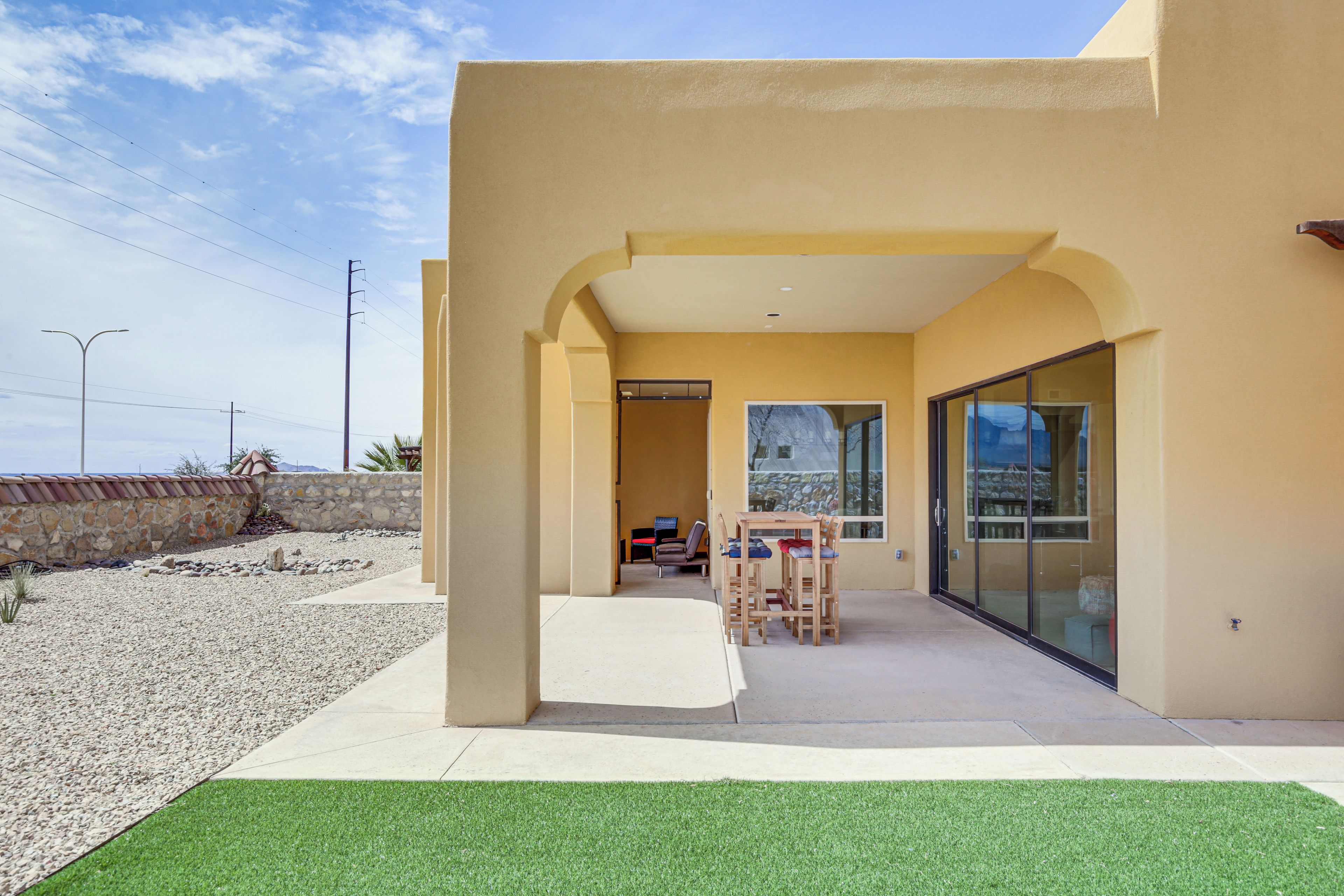 A modern building with a patio area featuring a table and chairs, a glass door, and a view of the surrounding landscape.