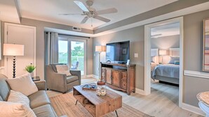 A modern living room with a sofa, coffee table, and TV. There is a balcony with a view of the outdoors. - Summerhouse Villas Condo With Resort Amenities! (Pawleys Island)