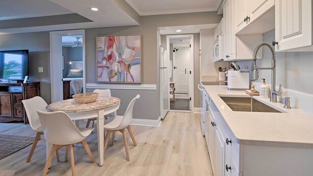 A modern kitchen with white cabinets, a large island with a sink, and a dining area with a round table and chairs. - Summerhouse Villas Condo With Resort Amenities! (Pawleys Island)