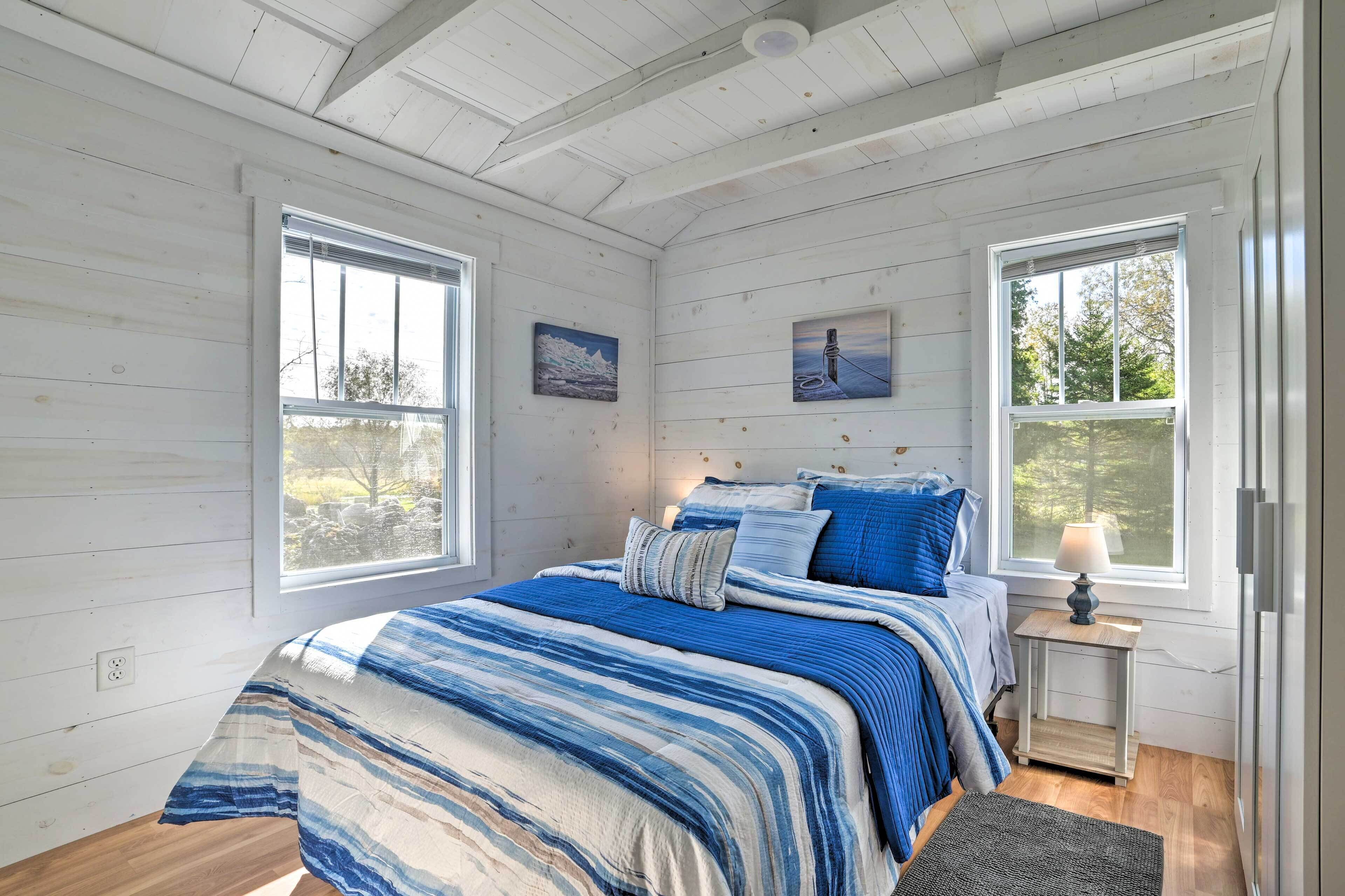 A bedroom with a bed, two windows, and a nightstand with a lamp.