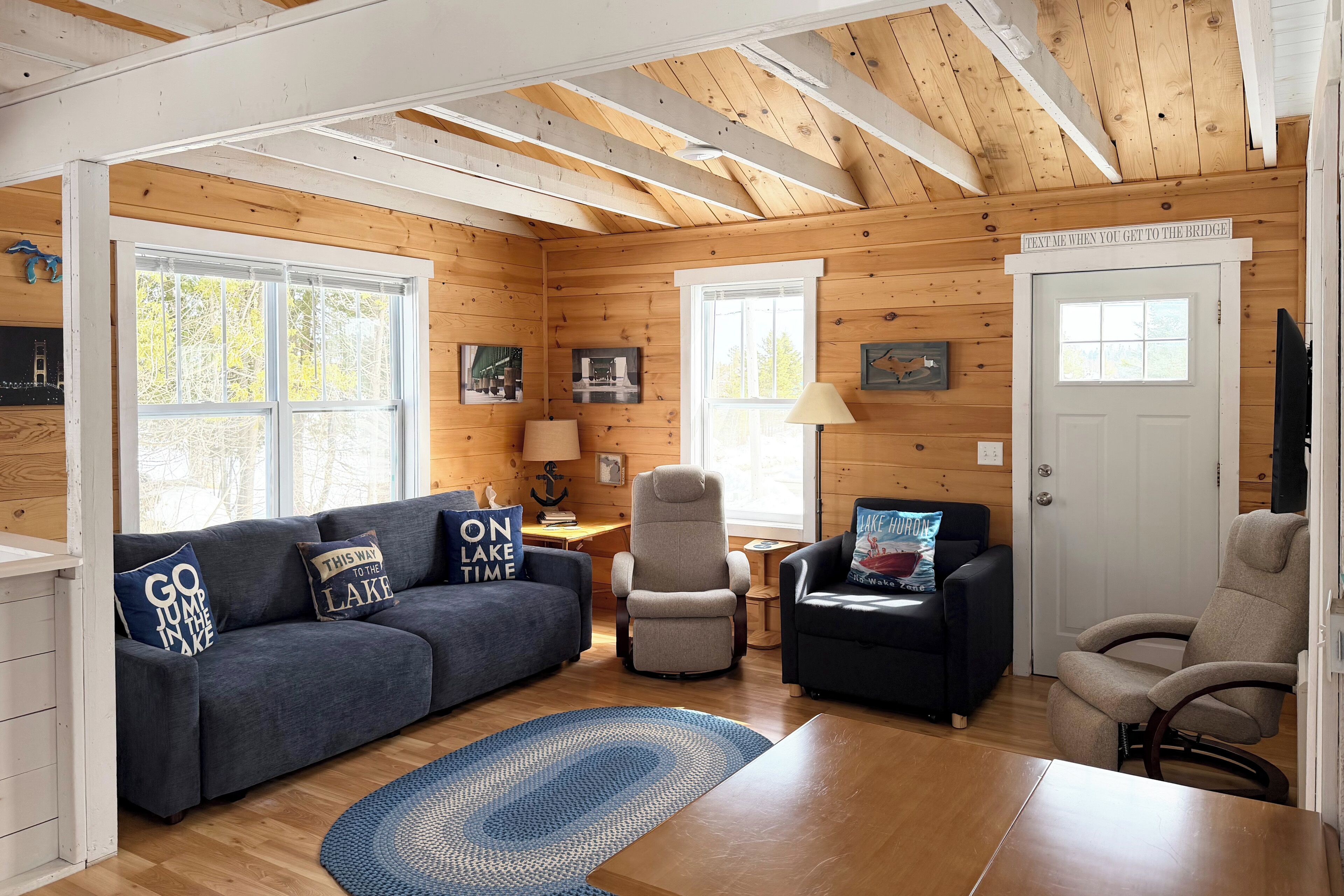 A cozy cabin interior with a sofa, armchairs, a table, and a fireplace.