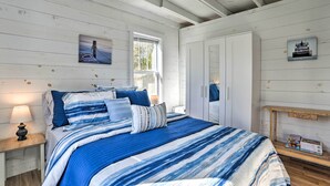 A bedroom with a bed, a nightstand, a wooden bench, and a window. - Cozy Cedarville Cottage - Walk to Lake Huron! (Cedarville)