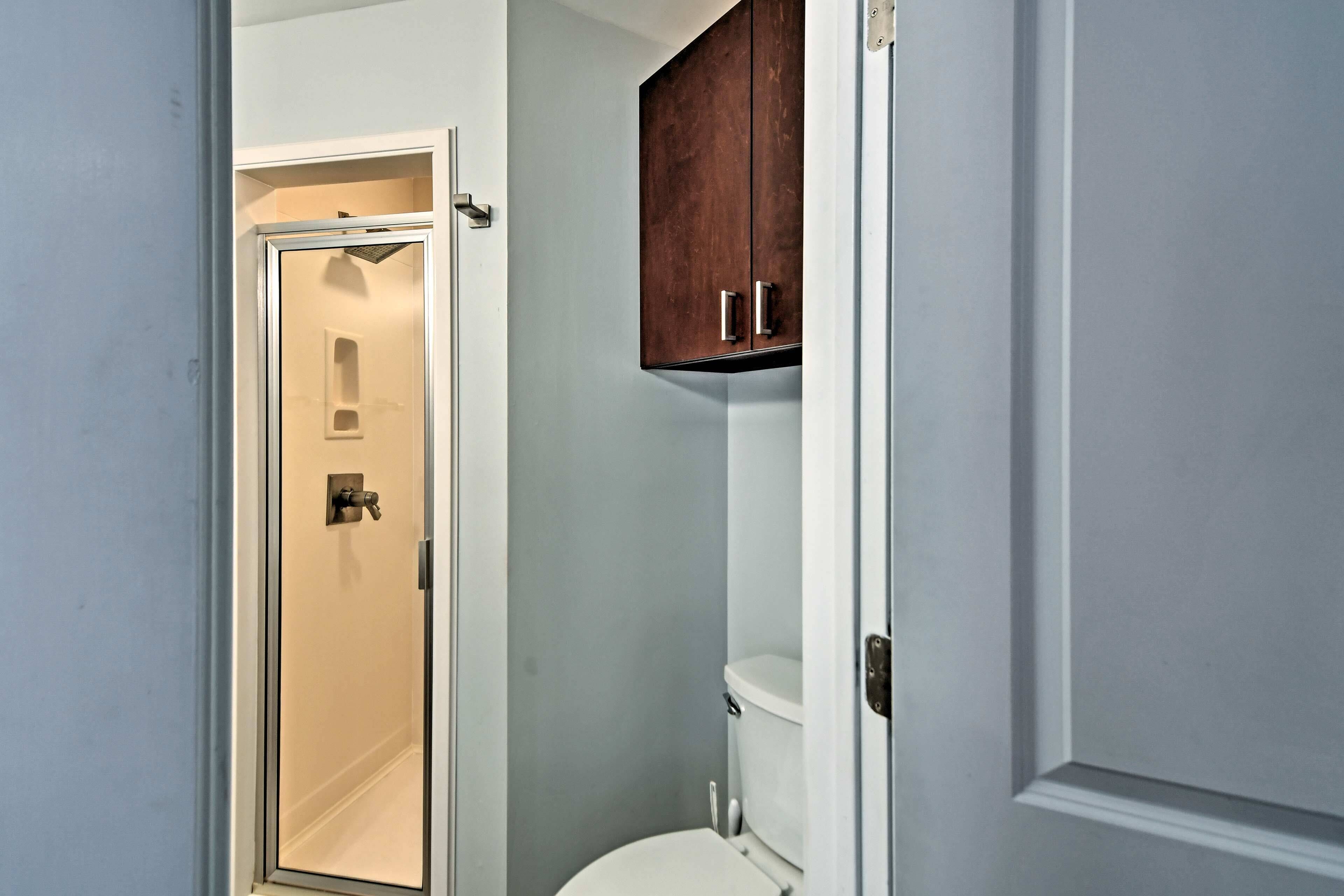 Un baño con ducha, inodoro y un armario de madera sobre el inodoro.