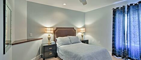 A bedroom with a bed, nightstands, lamps, a ceiling fan, and curtains.