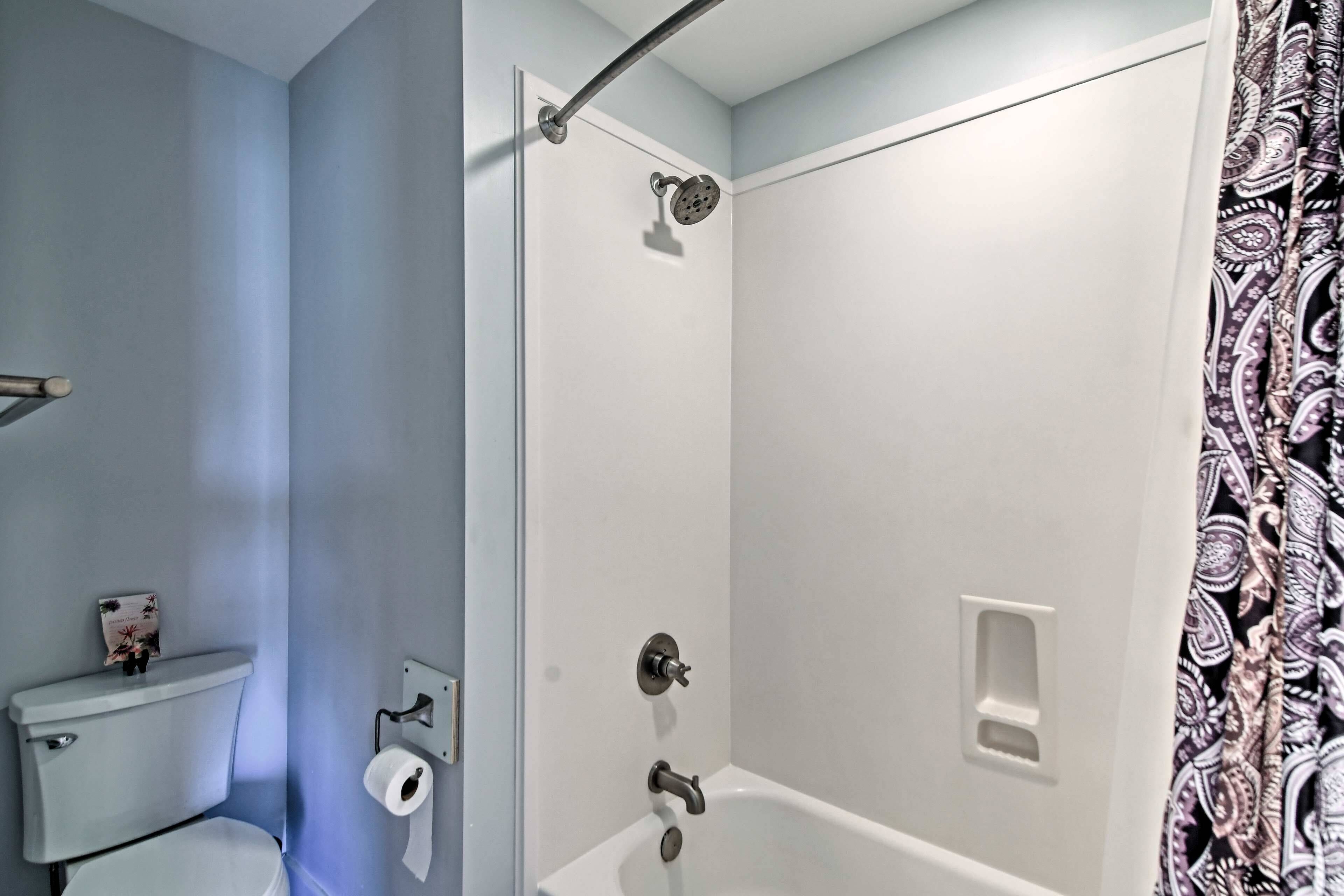 A bathroom with a toilet, a shower, and a roll of toilet paper on the wall.