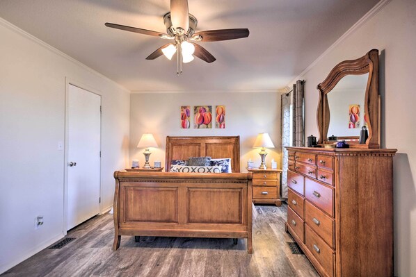 A bedroom with a wooden bed, two bedside tables with lamps, a dresser, and a ceiling fan.