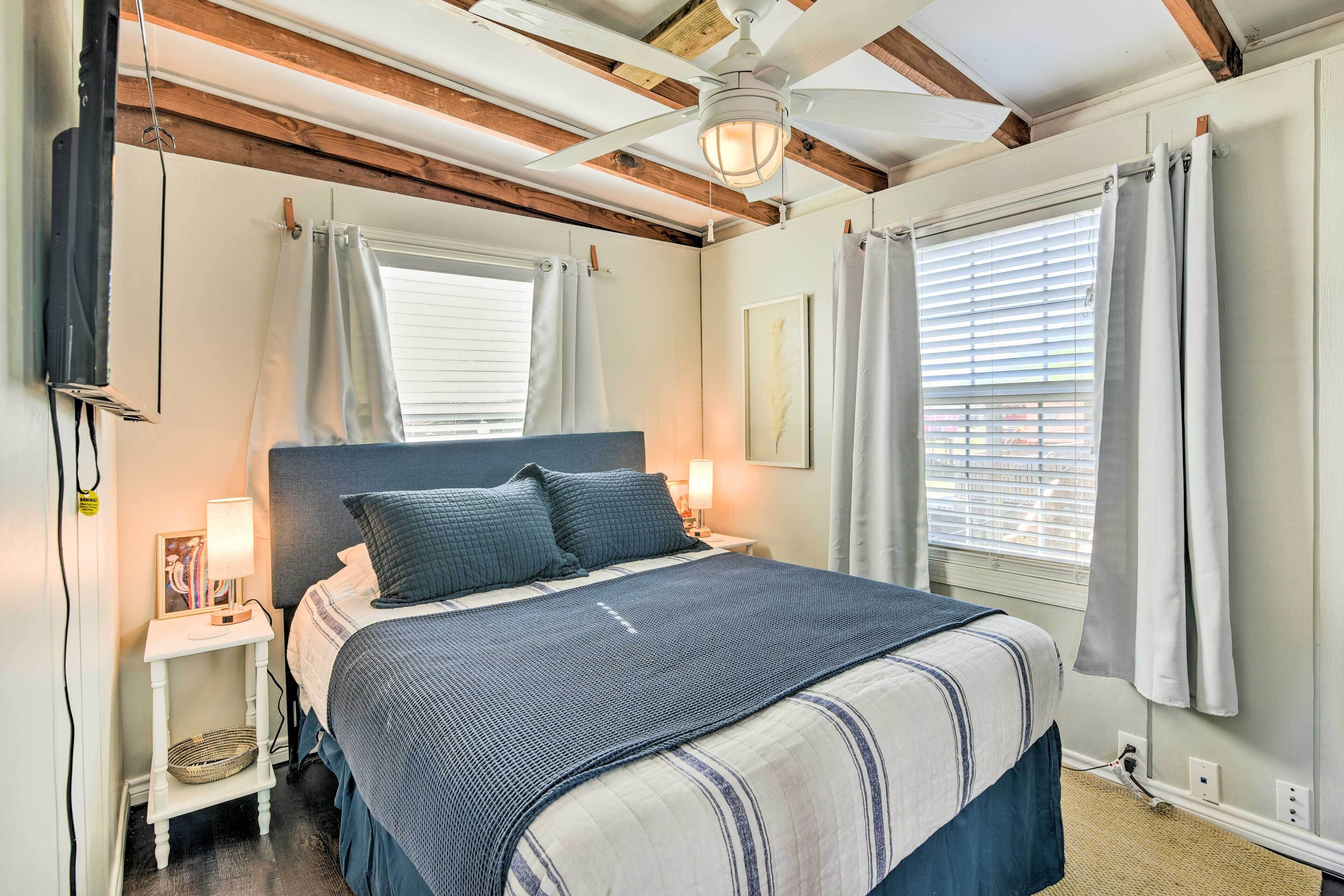 A bedroom with a bed, bedside tables, a ceiling fan, and windows with curtains.