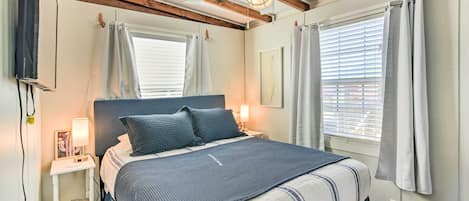 A bedroom with a bed, bedside tables, a ceiling fan, and windows with curtains.