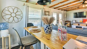 Een eetruimte met een houten tafel, stoelen, een vaas met gedroogde planten, een waterdispenser en een televisietoestel op de achtergrond.