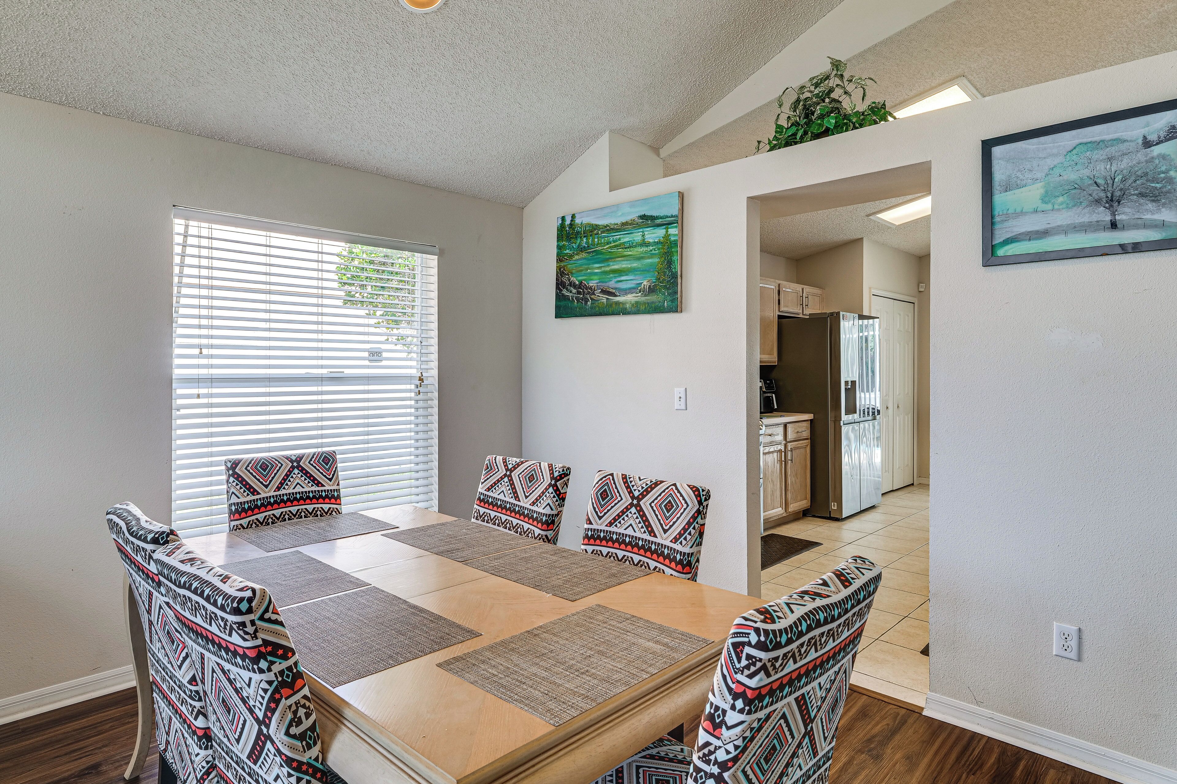 A dining area with a wooden table, patterned chairs, and a view into the kitchen.