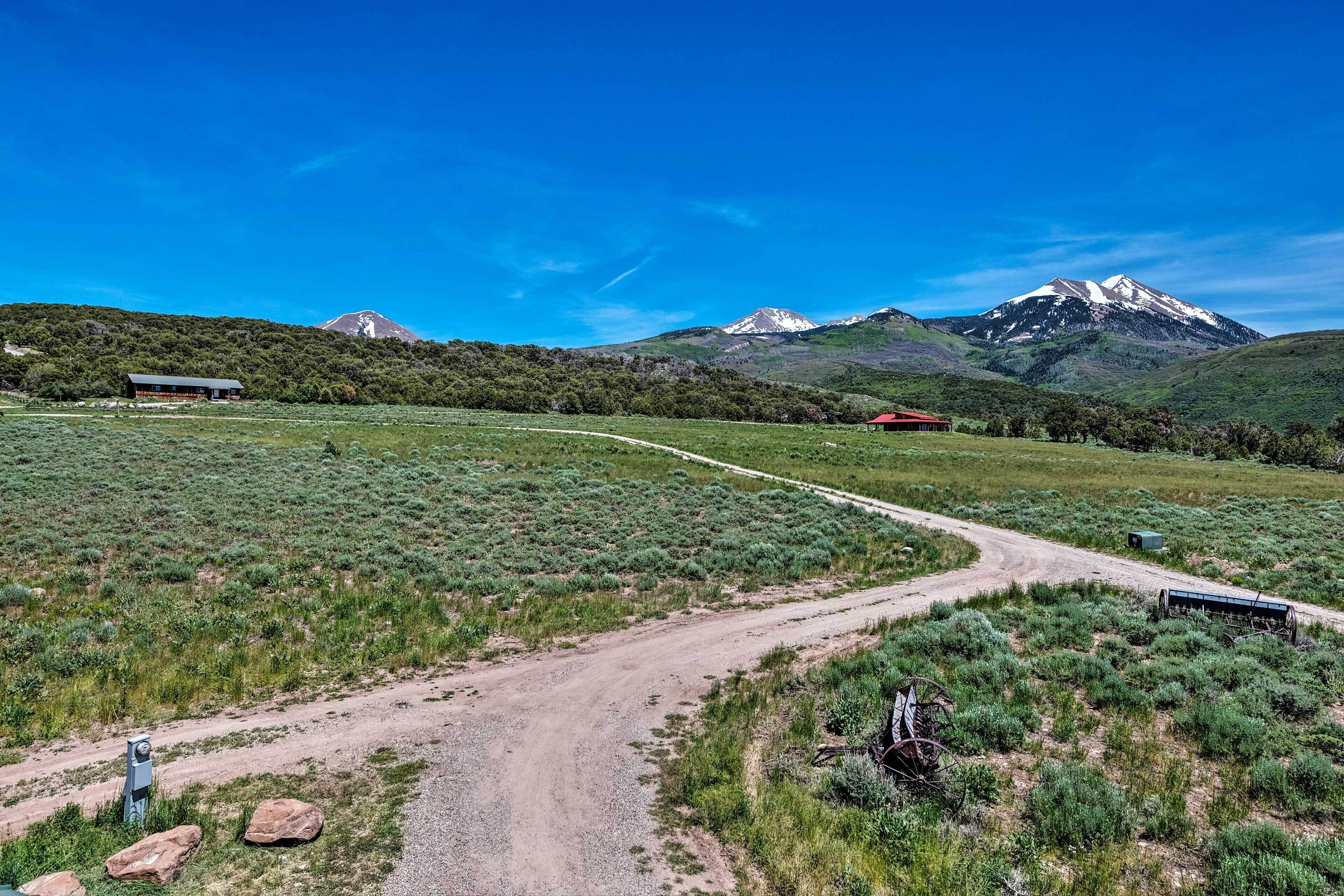 A rural landscape with a dirt road, a windmill, and a mountain range in the background.