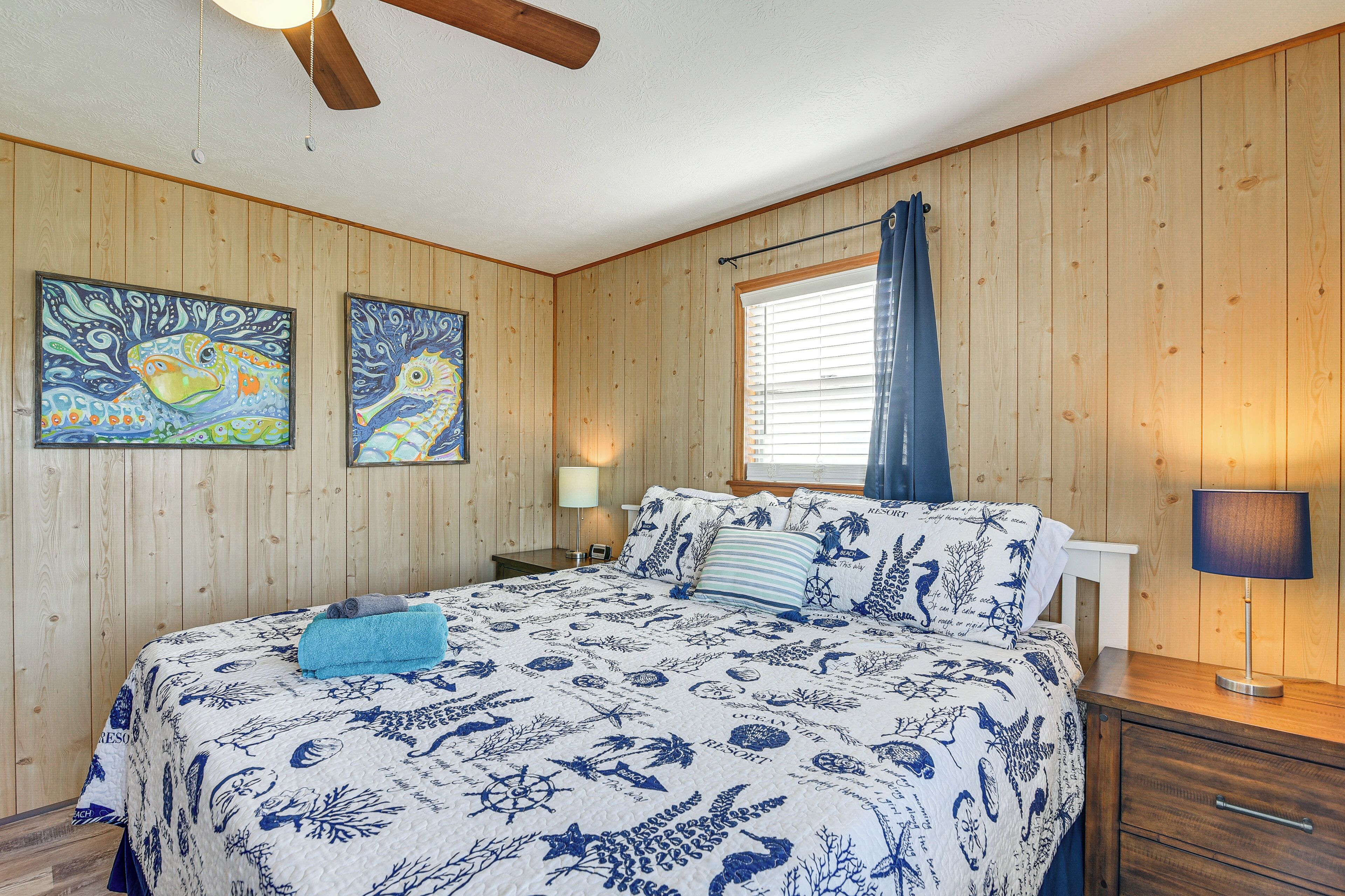 Una habitación con paneles de madera, una cama, una mesita de noche, una lámpara y dos cuadros en la pared.