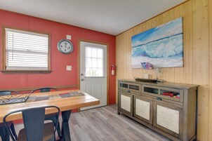 Un comedor con una mesa y sillas de madera, un reloj en la pared y un cuadro de una playa.
