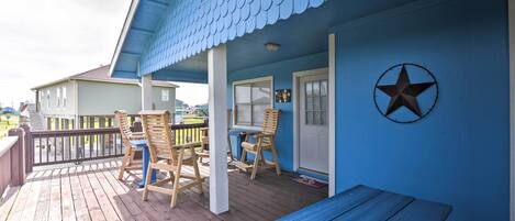 A blue house with a wooden deck, a bench, and two chairs.