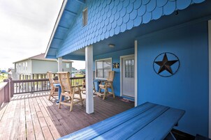 Una casa azul con terraza de madera, un banco y dos sillas.