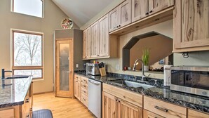 A kitchen with wooden cabinets, granite countertops, a dishwasher, and a large window. - Spacious & Secluded Home by Pokegama Lake! (Cohasset)