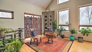 A spacious living room with a high ceiling, large windows, a decorative wooden screen, a round coffee table, and multiple potted plants. - Spacious & Secluded Home by Pokegama Lake! (Cohasset)