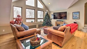 A spacious living room with leather sofas, a glass coffee table, a Christmas tree, and a large window overlooking a snowy landscape. - Spacious & Secluded Home by Pokegama Lake! (Cohasset)