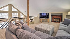 A spacious living room with a large window, a television, a fireplace, and a staircase leading to an upper level. - Spacious & Secluded Home by Pokegama Lake! (Cohasset)