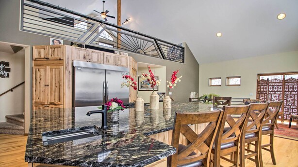 A kitchen with a granite countertop, wooden cabinets, a stainless steel refrigerator, and a dining area with wooden chairs. - Spacious & Secluded Home by Pokegama Lake! (Cohasset)