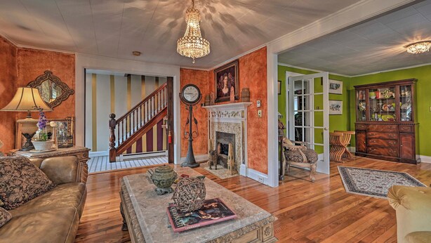 A spacious living room with a fireplace, a chandelier, and a staircase leading to another room. - Unique & Historic Home Walk to Lake Champlain (Plattsburgh)