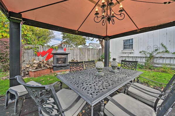 An outdoor patio with a metal table and chairs, a decorative chandelier, and a wooden fence in the background. - Unique & Historic Home Walk to Lake Champlain (Plattsburgh)
