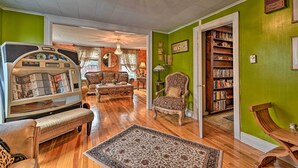 A living room with a jukebox, a patterned rug, and a bookshelf. - Unique & Historic Home Walk to Lake Champlain (Plattsburgh)