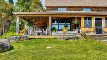 A wooden house with a covered porch, large windows, and a well-maintained lawn.