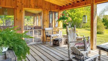 A wooden deck with outdoor furniture, including chairs and a table, overlooking a garden.