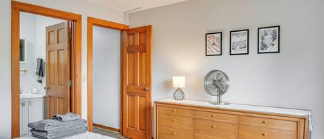 A bedroom with a bed, a wooden dresser, a fan, and three framed pictures on the wall.