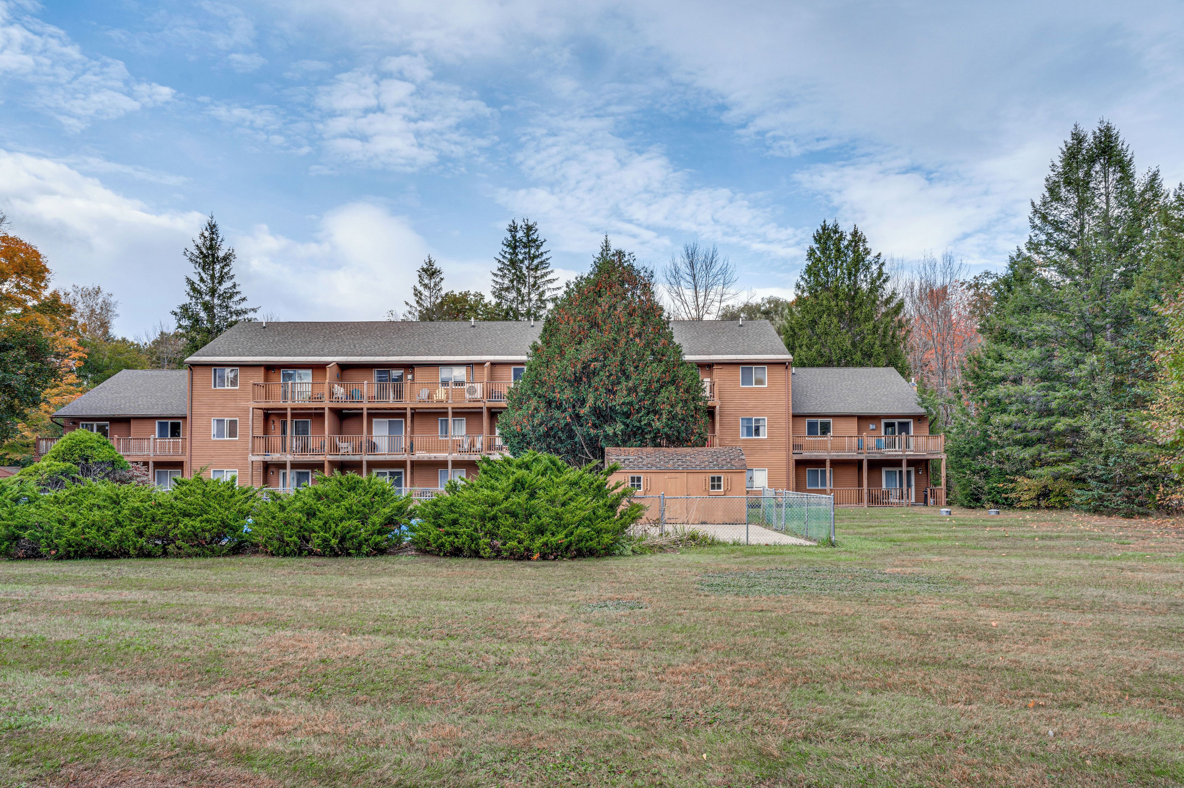 A multi-story apartment building with balconies, surrounded by a grassy area and trees.