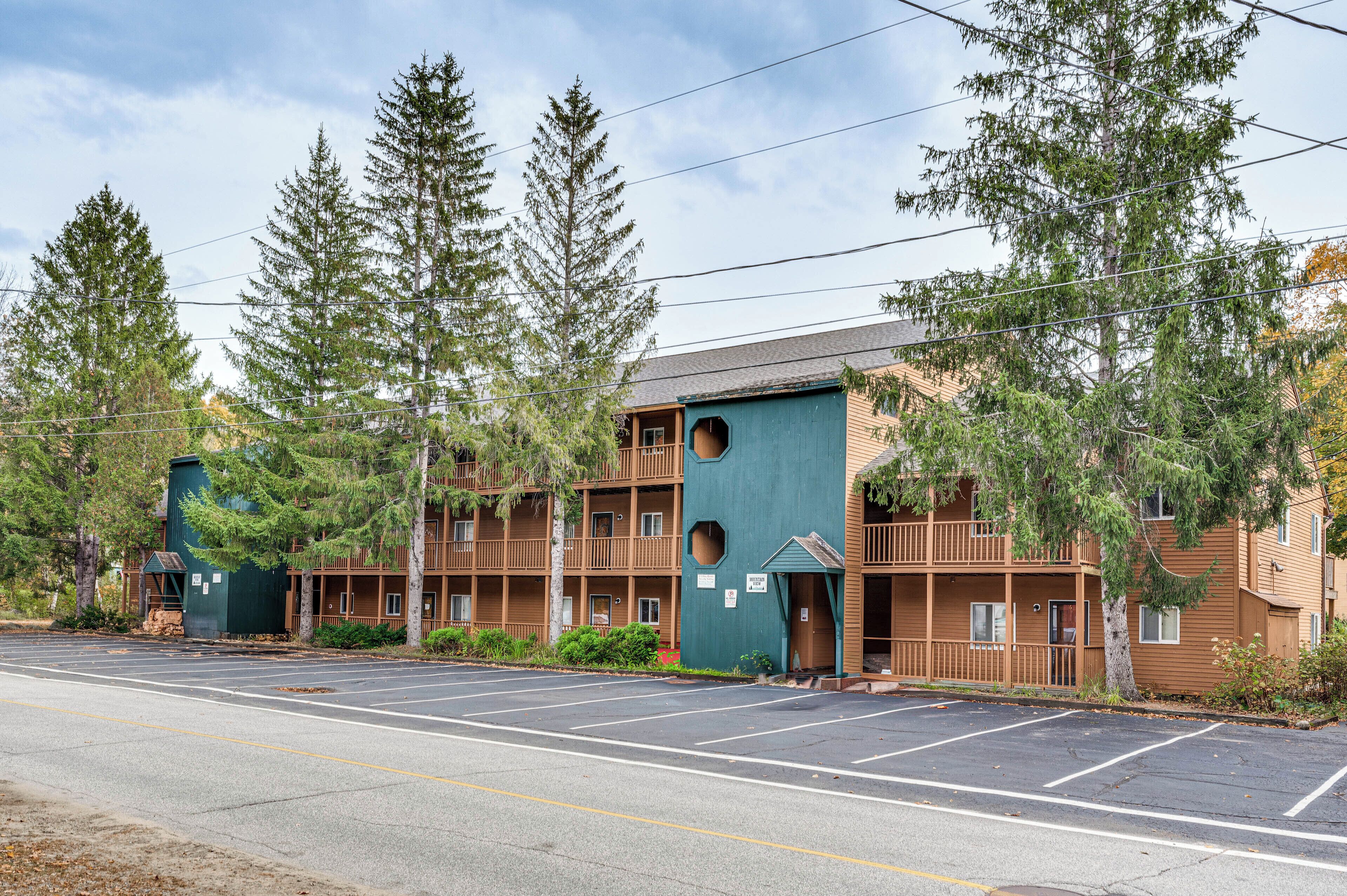 A multi-story motel with a distinctive green and brown facade, featuring balconies and a parking lot in front.