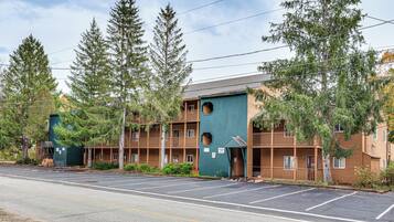 A multi-story motel with a distinctive green and brown facade, featuring balconies and a parking lot in front.