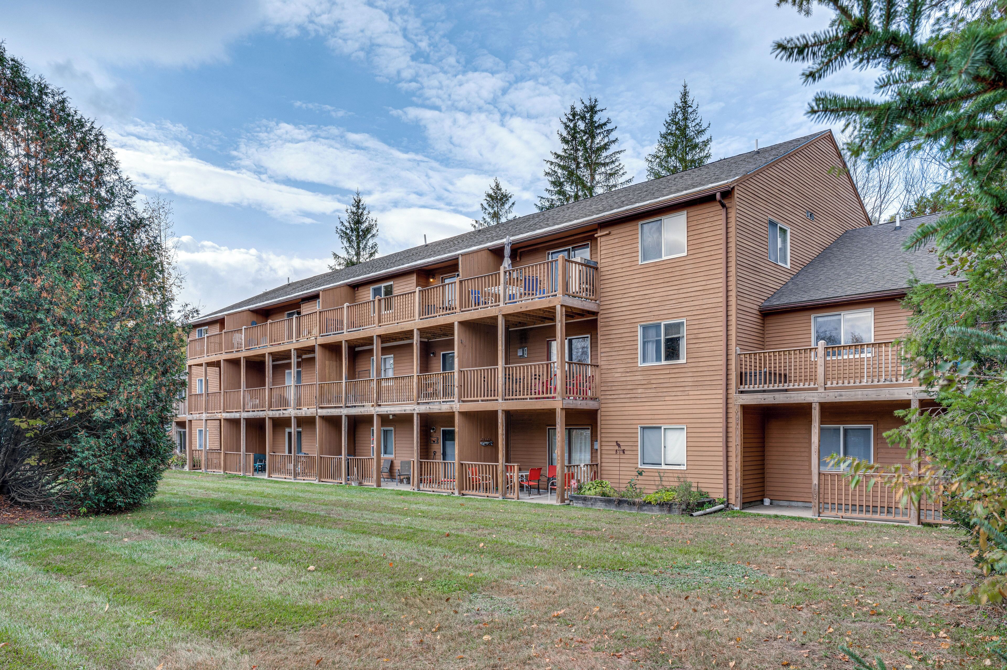 Un edificio de apartamentos de madera de varios pisos con balcones, un césped y árboles circundantes.