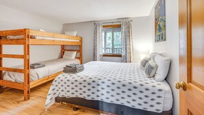 Ein Zimmer mit einem Etagenbett, einem Einzelbett, einem Fenster mit Vorhängen und einer Tür.