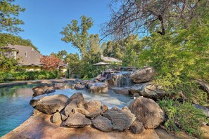 Zona de piscina natural con cascada, rodeada de rocas y vegetación.
