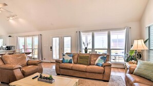 A spacious living room with a brown leather sofa, a white coffee table, and a dining area with a table and chairs. - Walk to Ocean: Coastal Home in Crystal Beach! (Port Bolivar)