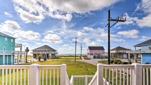 A coastal residential area with houses, a grassy lawn, and a wooden deck with white railings. - Walk to Ocean: Coastal Home in Crystal Beach! (Port Bolivar)