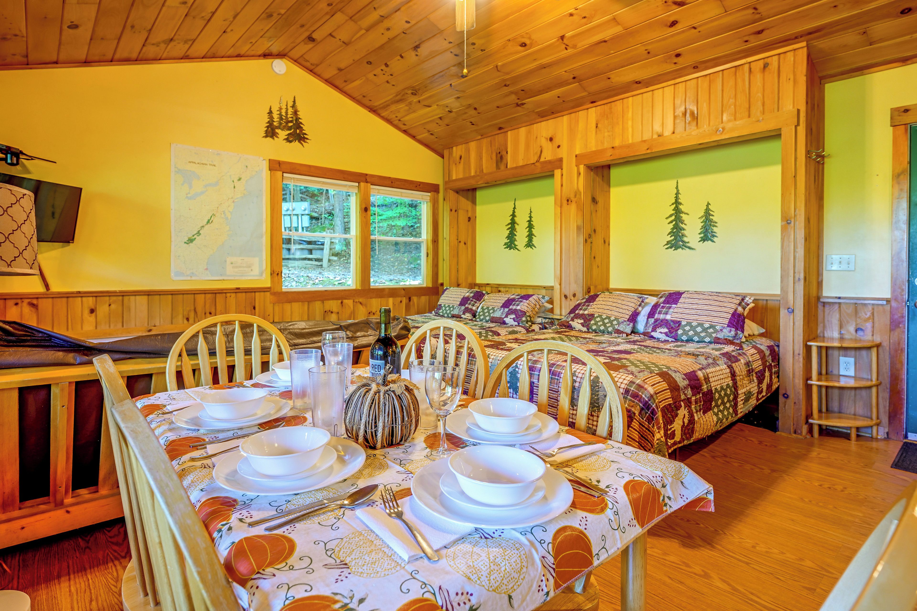 A cozy cabin interior with a dining area, a bed with a colorful quilt, and a map on the wall.