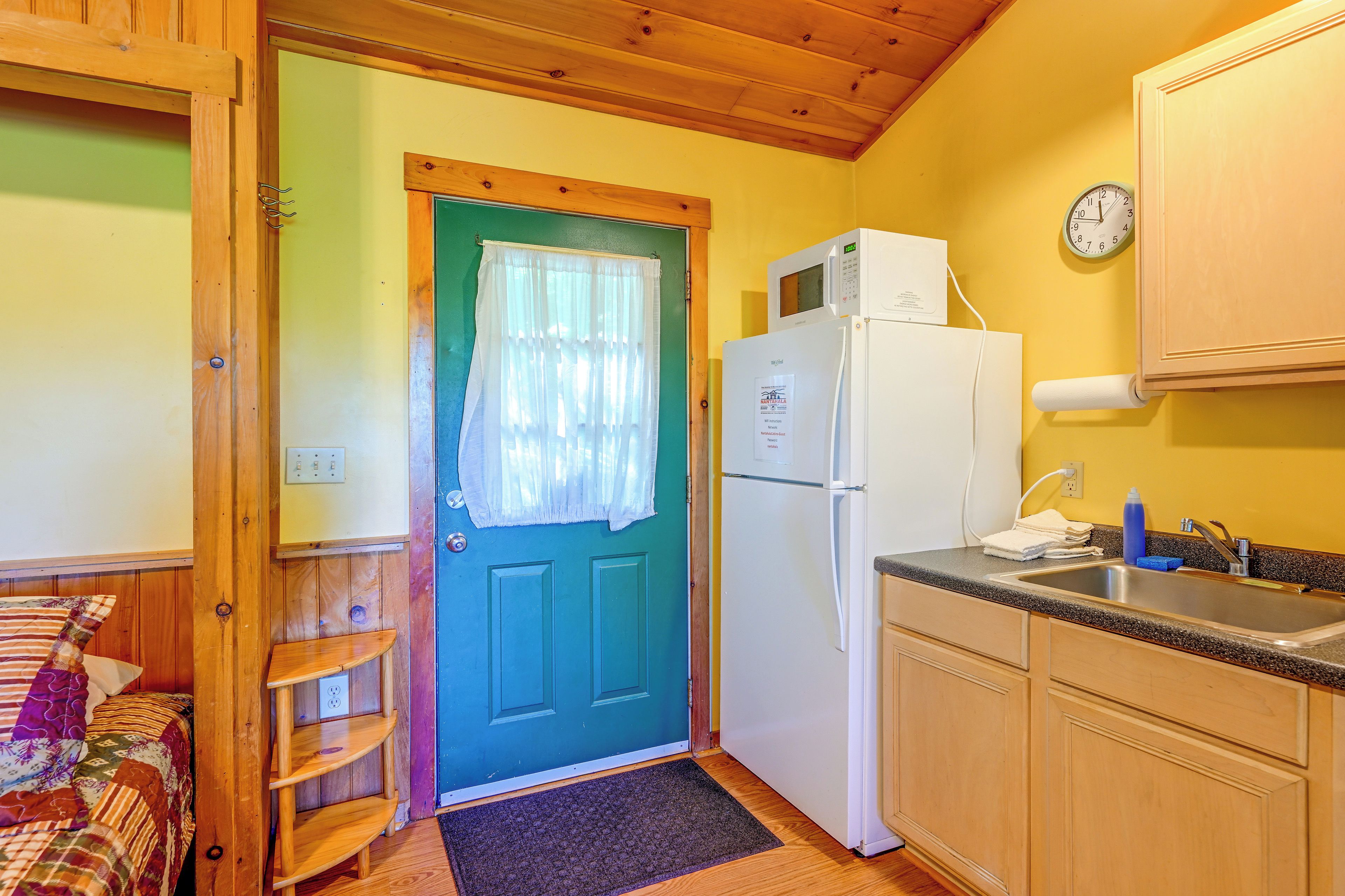 A compact kitchen with a refrigerator, microwave, and a clock on the wall.