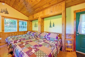 A wooden cabin bedroom with two beds, a green door, and windows with forest views.
