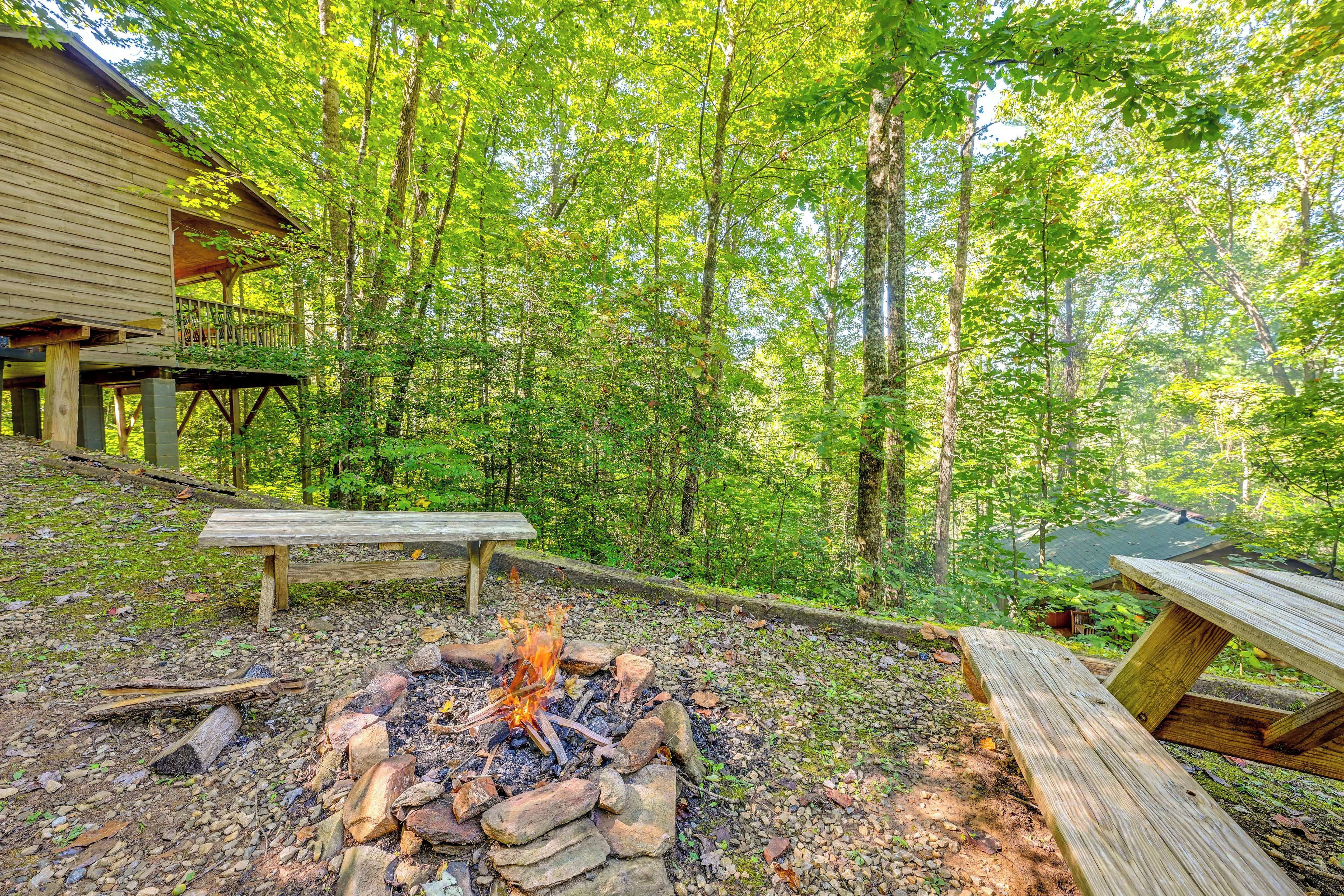 A wooden deck with a fire pit and picnic table in a forested area.