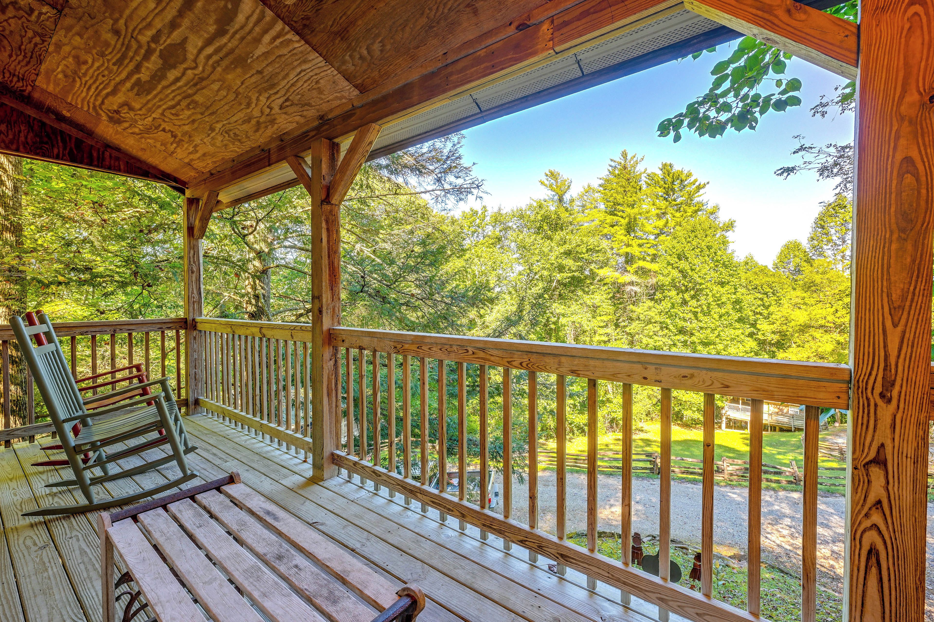 A wooden deck with a railing, a bench, and a view of a forested area.