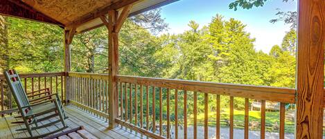 A wooden deck with a railing, a bench, and a view of a forested area.